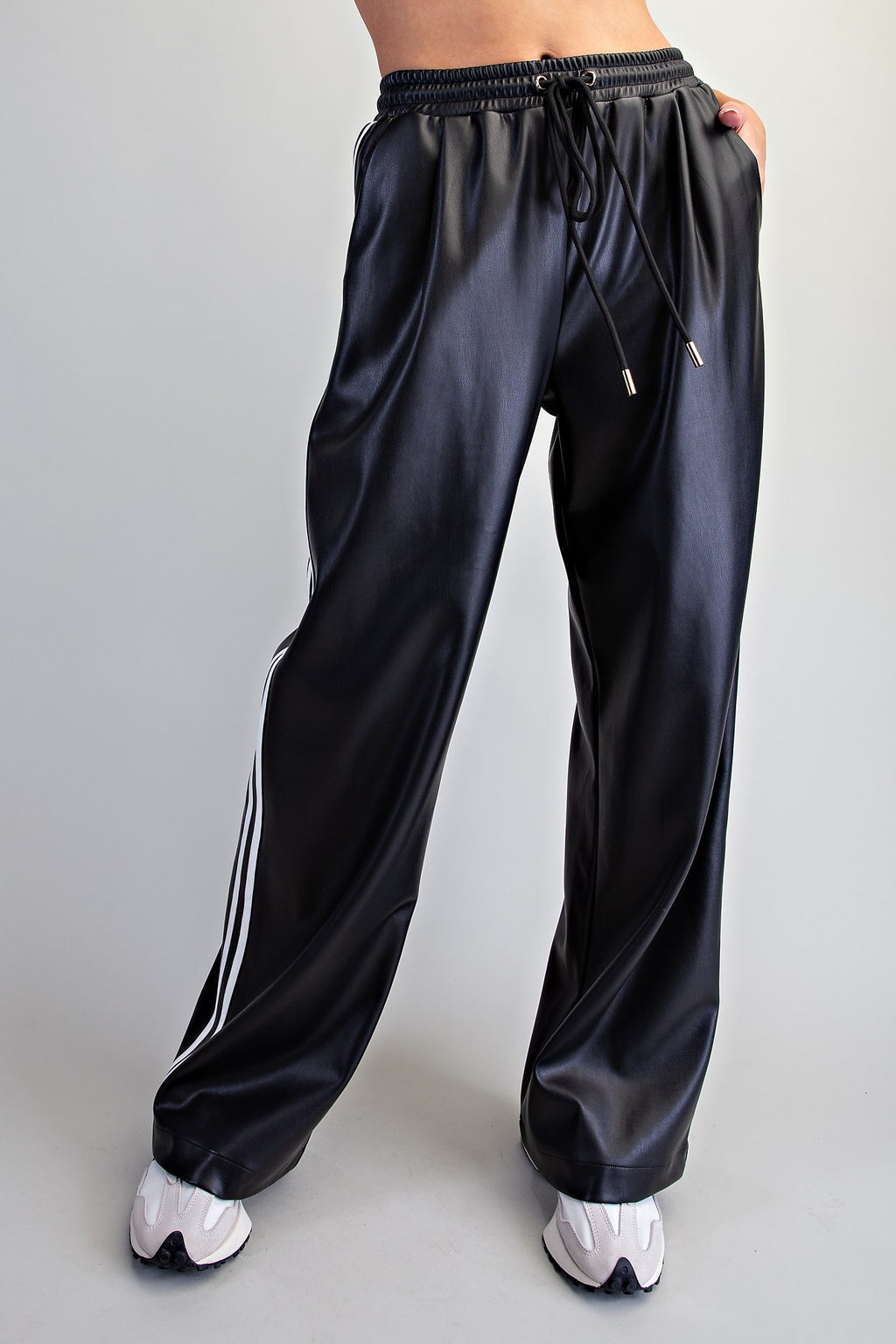 Black faux leather wide-leg pants with white side stripes, styled with sneakers.