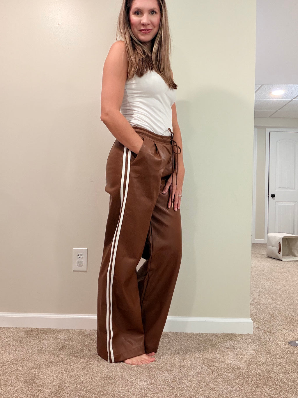 Side view of chocolate brown faux leather pants showing cream double stripes and a side pocket.